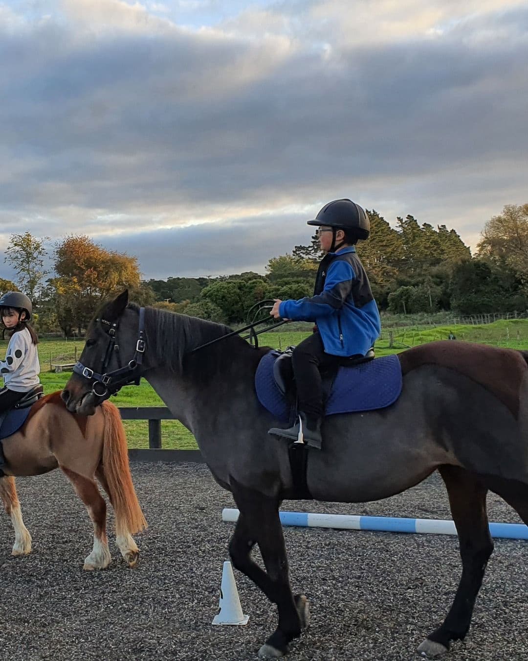 Two riders on horseback in the arena in the last light of the afternoon
