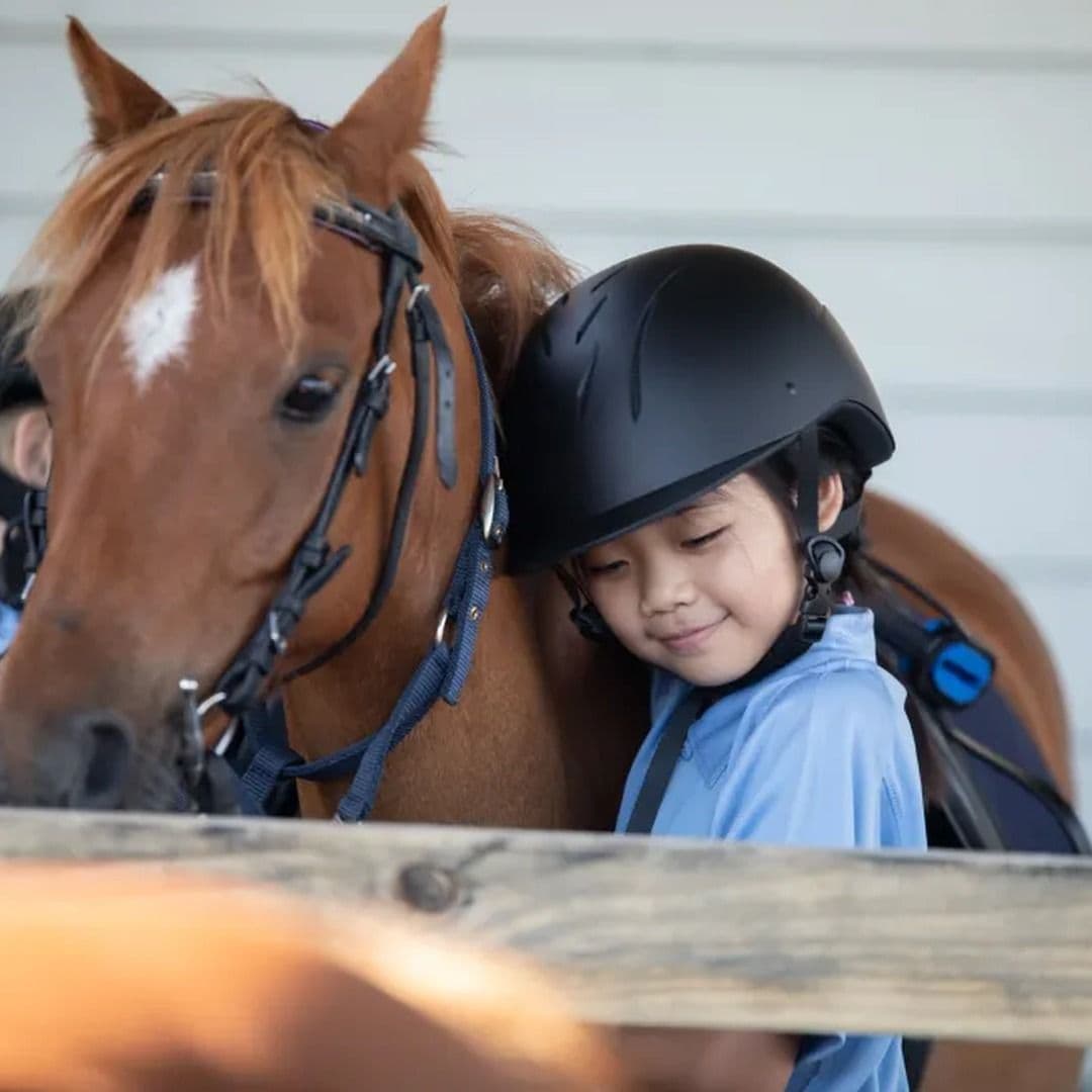 A young rider resting their head against a chestnut pony